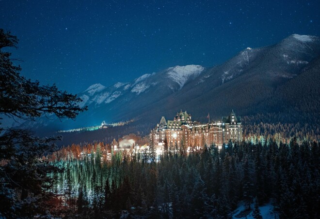 A night time view of the castle-like Fairmont Banff Springs hotel in Alberta surrounded by forests and mountains.