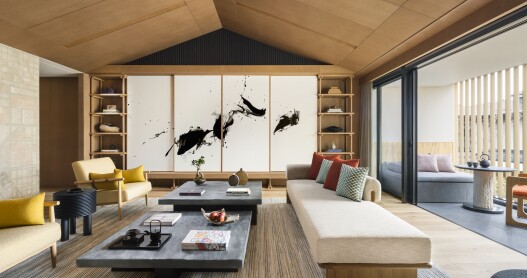 The living room of the Three Bedroom Penthouse Suite at the Six Senses Kyoto features a large black and white brush painting,  large white sofas, and a large terrace.