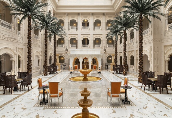 This public space at the Raffles Jaipur in Rajasthan has large palm trees and scalloped arches, with a gold fountain at its center.