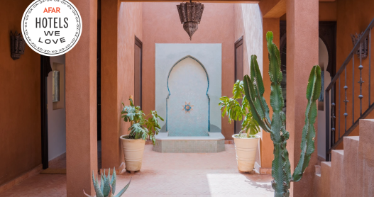 The courtyard of a riad at Kasbah Tamadot in Morocco with pink walls, cacti, and a metal chandelier.