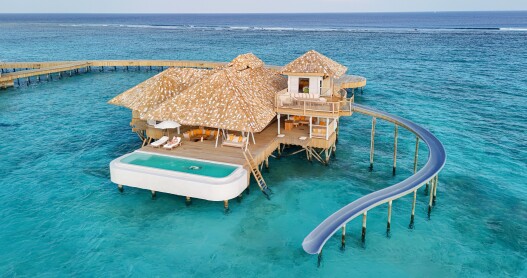 A villa at Soneva Secret in the Maldives with thatched roofs and a waterslide.